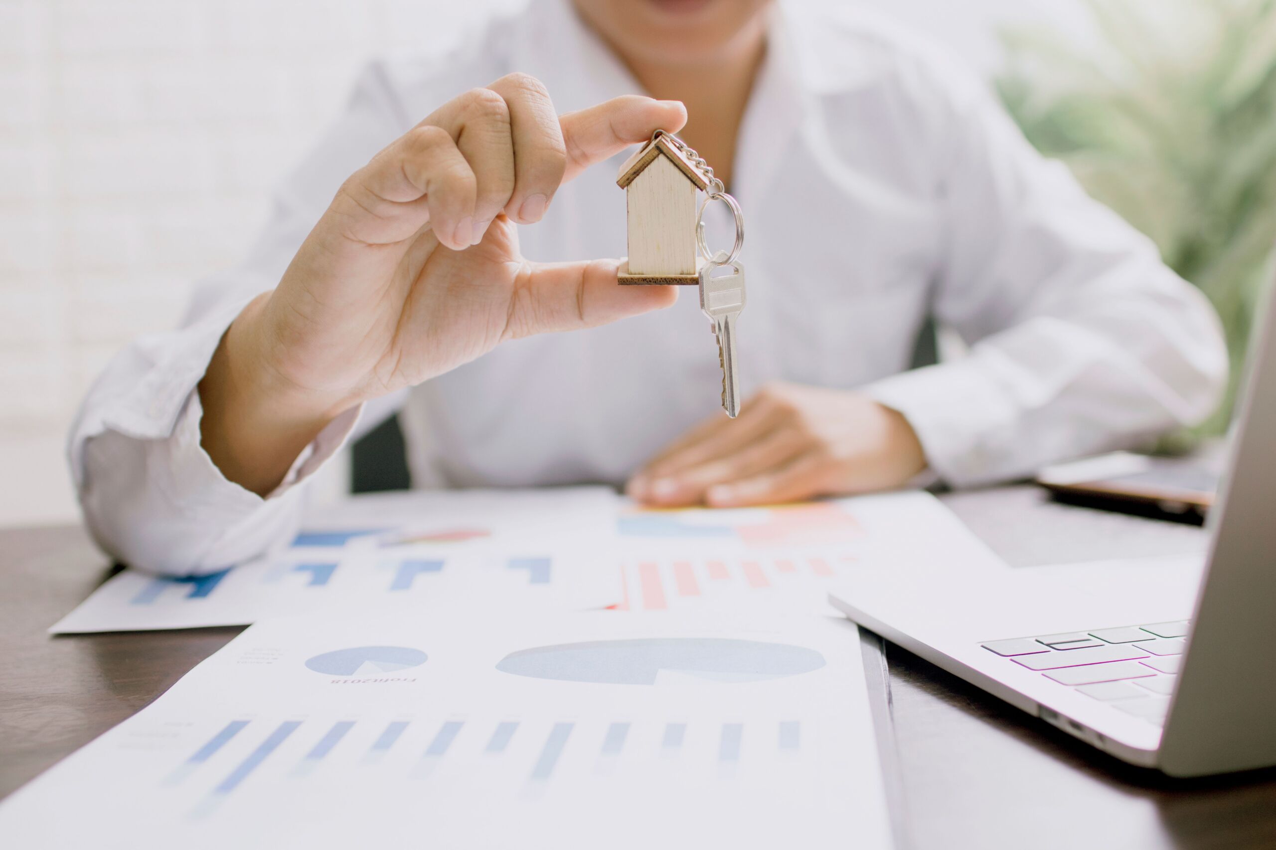 a person in white long sleeves holding a house keychain with a key
