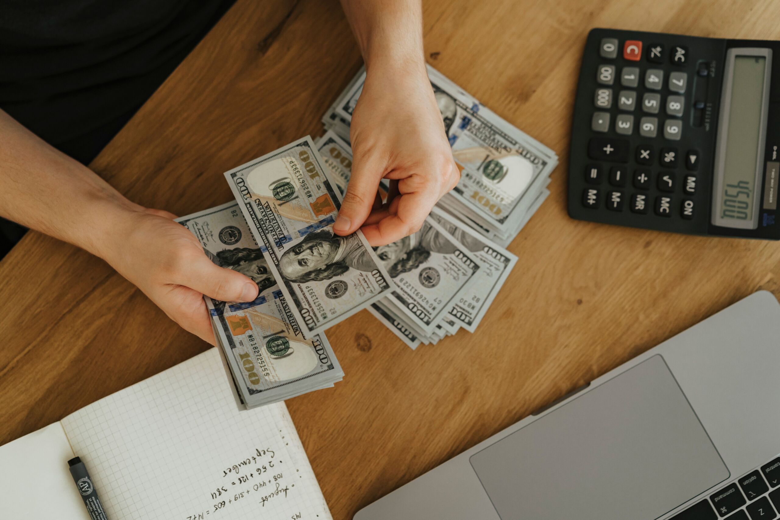 a person holding money near a calculator and laptop